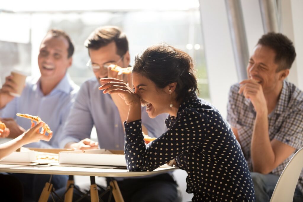 Glückliche zufriedene Mitarbeiter lachend an einem Tisch mit Pizza