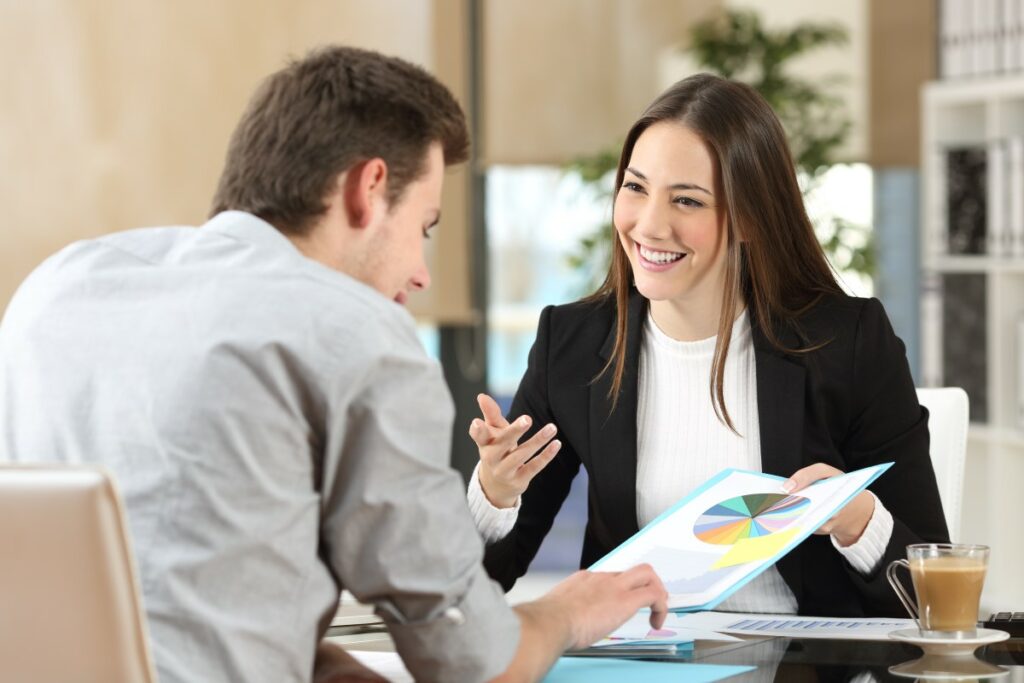 Frau im Business Look sitzt am Tisch und zeigt Ihrem Kollegen ein Feedback Chart