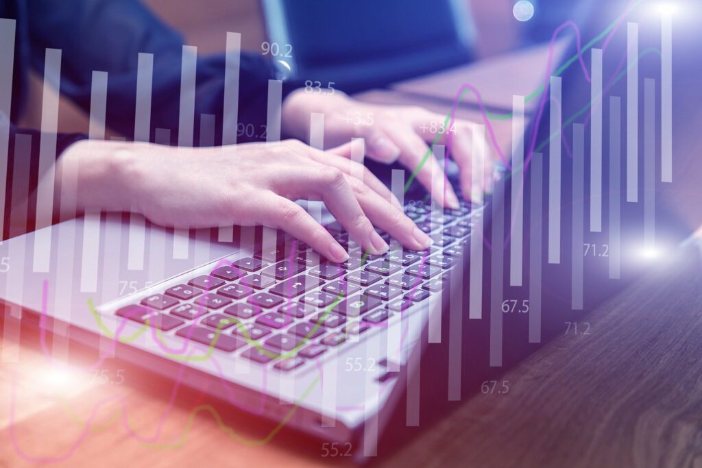 Laptop, zwei Hände tippen darauf, darüber Statistiken