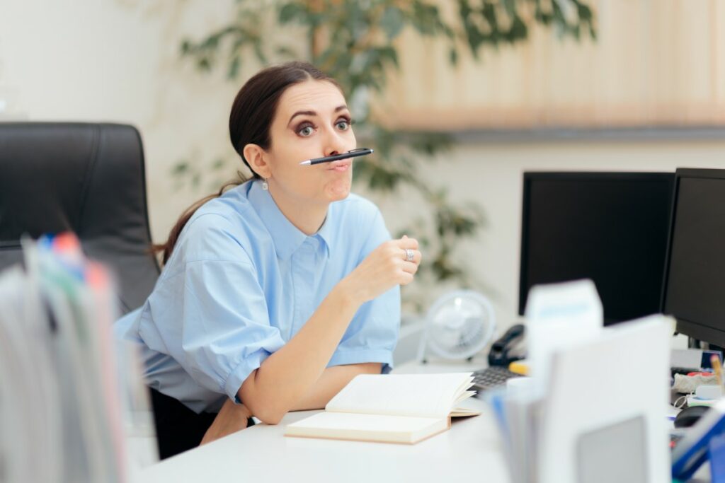Mitarbeiterin sitzt am Schreibtisch, denkt über Kündigung nach, Stift zwischen Lippen und Nase geklemmt
