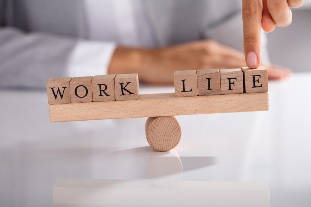 Waage mit Holzklötzen mit Schrift Work Life Balance, Finger drückt von oben auf Seite mit &quot;Life&quot;
