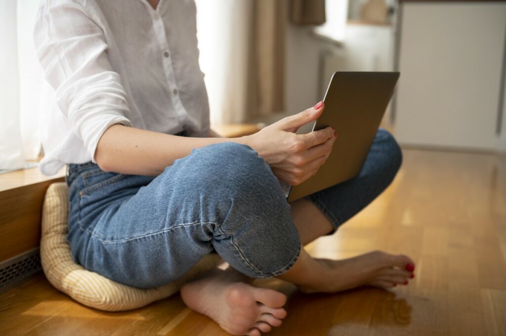 Frau mit Laptop arbeitet mit verschränkten Beinen auf dem Boden in ihrer Wohnung