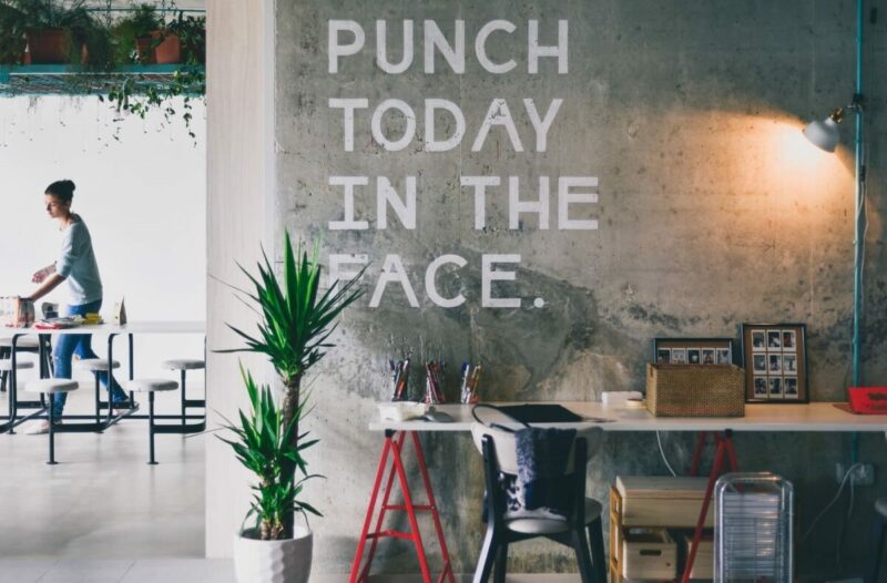 Coworking Space mit Schriftzug an der Wand: &quot;Punch today in the face&quot;. Symbolbild für Mitarbeitermotivation steigern, Produktivität steigern