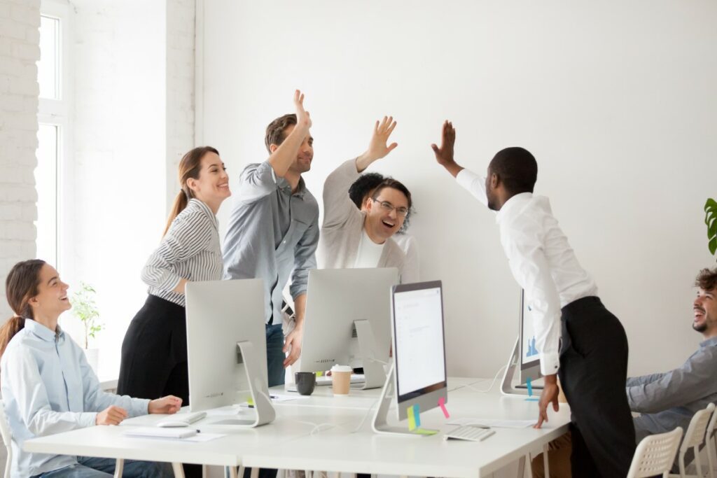 Personen verschiedenen Geschlechts und Alters stehen im Büro einer Organisation um eine Arbeitsplatz Insel und geben sich High Five