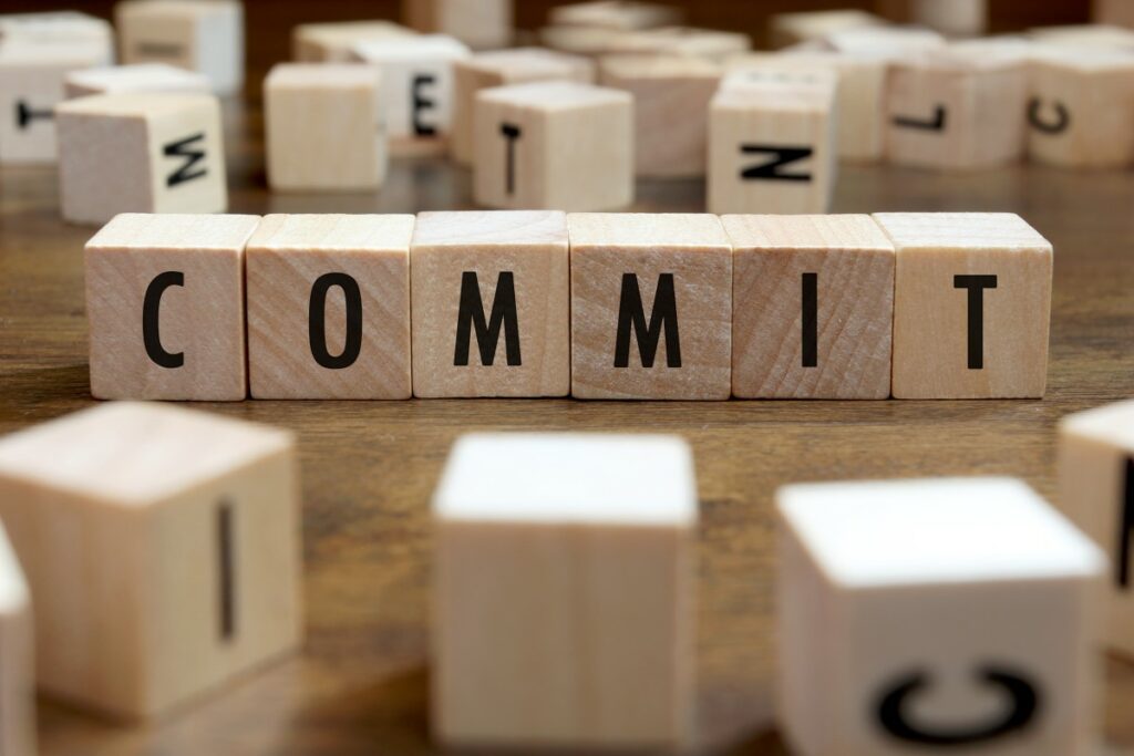 Holzwürfel mit großen schwarzen Buchstaben ergeben den Anfang des Worts Commitment