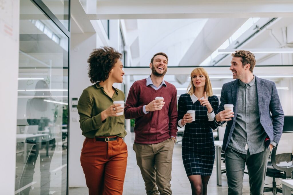 Vier Mitarbeiter und Mitarbeiterinnen unterhalten sich auf dem Gang mit Kaffee engagiert über das Business