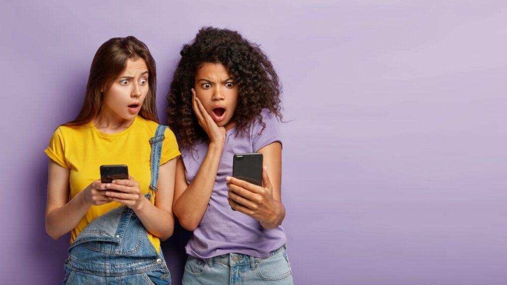 Zwei Frauen schauen schockiert nach Mitarbeiterbefragung auf ihre Smartphones