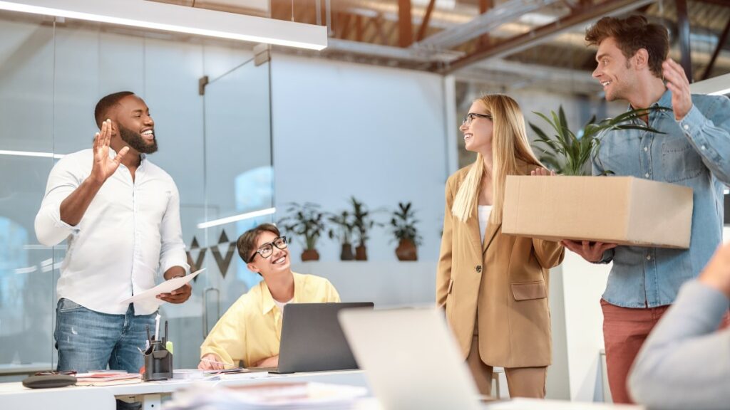 mann am ersten tag im büro mit einem karton wird von kollegen gegrüßt