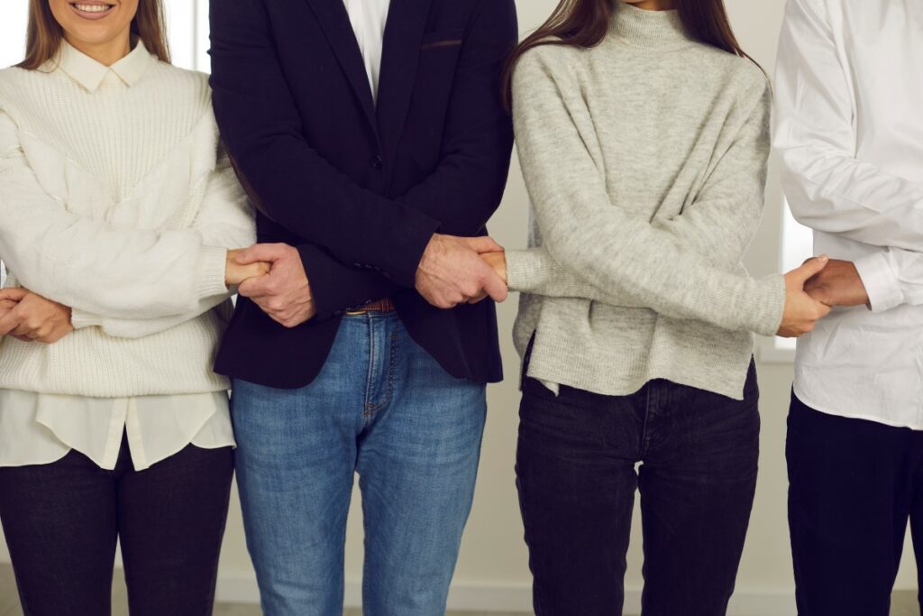 Vier treue Mitarbeiter halten die Hände vor dem Bauch über Kreuz und halten sich an den Händen